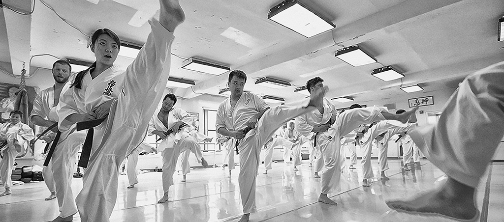 Rows of Kyokushin students in white gi training together in the dojo